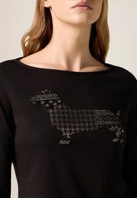 Czarny top z tkaniny z motywem jamnika wykonanym z teksturowanego, czarnego materiału w jodełkę z błyszczącymi akcentami oraz okrągłym dekoltem.