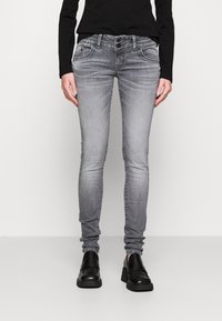Gray skinny jeans made of denim with a slight fade, mid-rise waist, secured with two buttons, and five-pocket style. Worn with black loafers.
