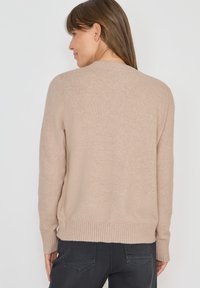 Ljusbeige tröja i mjukt material, med rund halsringning, ribbade ärmslut och nederkant, med en avslappnad passform och sidoöppningar.
