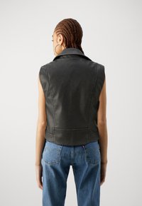 Svart läderväst utan ärmar med spetsig krage och figursydd design, parat med högmidjade blå denimjeans.