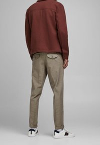 Bordowa polarowa kurtka, beżowe spodnie w paski oraz białe trampki z granatowymi i czerwonymi akcentami. Charakterystyczne detale to naszywane kieszenie.