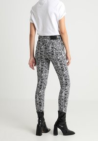 Leggings de estampado de serpiente en blanco y negro, diseño ajustado, material elástico, cintura alta, combinados con botas de tacón negras y una camiseta blanca.
