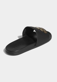 Černé skluzavkové sandály vyrobené z hladké kůže s širokým páskem zdobeným zlatým logem. Plochá podešev s texturovaným povrchem pro lepší přilnavost.