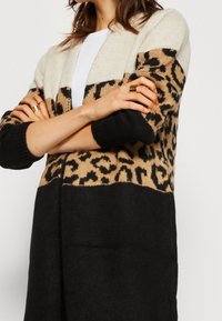 Gebreide cardigan met blokkleuren: crème, beige luipaardprint en zwart. Lange mouwen met ribbelmanchetten, open voorkant. Zachte textuur.