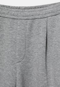 Sive trenirke, narejene iz mehkega, teksturiranega blaga, imajo elastičen pas, detajle nabiranja in stranski žep. Površina se zdi rahlo melirana.