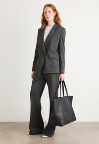 Costume ajusté en tartan gris avec un pantalon à jambes larges, accompagné d'un sac fourre-tout en cuir noir. Haut blanc sous la veste.
