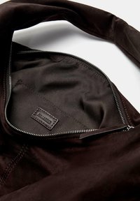 Wnętrze torby z ciemnobrązowego zamszu, wyposażone w gładką podszewkę materiałową oraz kieszeń na zamek z skórzaną metką. Miękka tekstura i prosty design.