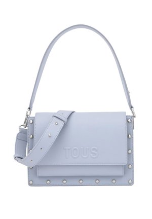 Persona con vaqueros azul claro y top de capas colorido sostiene un bolso TOUS de color lila claro con tachuelas por el asa.