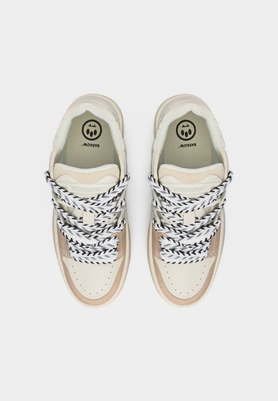 Μπεζ και άσπρα αθλητικά παπούτσια με κορδόνια ριγέ μαύρα και άσπρα, λεπτομέρειες από δίχτυ και λογότυπο της μάρκας στην περιοχή της φτέρνας, σε θέαση από πάνω.