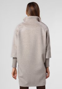 Maglione beige oversized con colletto alto a costine, maniche corte e un tessuto morbido e testurizzato, presenta una vestibilità rilassata e un design minimalista.