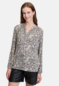 Langarmbluse mit floralem Muster in Creme und Marineblau, ausgestattet mit einem V-Ausschnitt und filigraner Stickerei entlang des Ausschnitts. Leichtes Material.