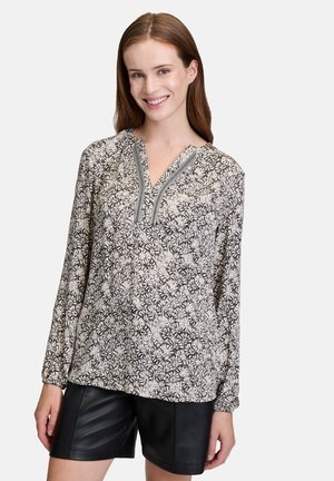 Blouse à manches longues avec un motif floral en crème et marine, dotée d'un col en V et de coutures intricacies le long du décolleté. Tissu léger.