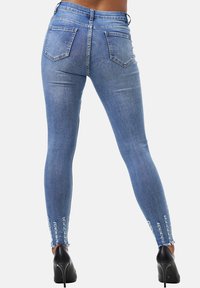 Vaqueros ajustados de color azul con una cintura de media altura, diseño de cinco bolsillos y detalles de dobladillo deshilachado. Presenta una textura de denim suave y un ajuste ceñido.