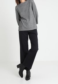 Graue strukturierte Langarmbluse mit weitem Ausschnitt, kombiniert mit lockeren schwarzen Hosen und schwarzen stiefelartigen Ankle Boots. Einfaches, lässiges Outfit.