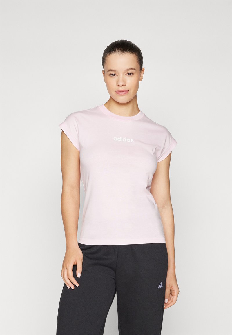 T-shirt de algodão rosa claro com mangas curtas enroladas e um logótipo branco "adidas" na frente, combinado com calças cinza-escuras.