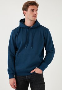 Marineblauer Kapuzenpullover mit einer Fronttasche, Kordelzug und gerippten Bündchen. Hergestellt aus glattem Stoff mit einem lässigen Schnitt.