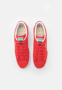 Punase dowd tõmmised suvekingad, millel on valged aktsendid, seotud disain, Puma logo keelel ja mustriline sisetall.
