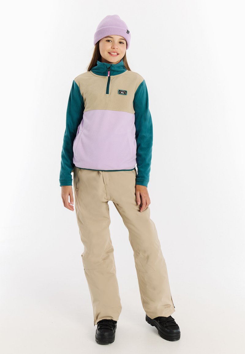 Fleecejack met een hoge kraag in lavendel, teal en tan, gecombineerd met beige broek. Het model draagt een lavendelkleurige beanie en zwarte laarzen.