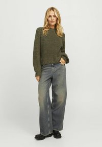 Olijfgroene gebreide trui met een losse pasvorm en ribbels aan de mouwen, gecombineerd met hooggewrongen wijde vervaagde blauwe jeans en zwarte platform schoenen.