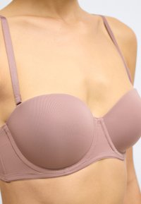 Formet stropfri bh i blødt mauve stof. Har glatte skåle, justerbare stropper og sømløse kanter for en ren finish.