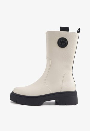 Valge nahast pahkluu saabas, millel on tekstuuriga viimistlus, tükk musta tallaga ja ringikujuline must logo küljes. Omab tõmbluku silmust lihtsaks selga panemiseks.