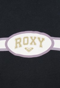 La tela negra presenta un logotipo ovalado blanco central con "ROXY" en dorado y un símbolo de corazón debajo, contorneado en lavanda clara.