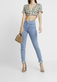 Top corto a cuadros en blanco y negro, jeans de tiro alto en azul claro, bolso de mano de serpiente beige y sandalias de tacón con tiras transparentes.