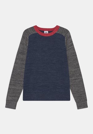 Długi sweter z okrągłym dekoltem, z granatowym korpusem, szarymi rękawami i czerwonym kołnierzem przy szyi.