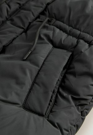 Schwarze Steppjacke aus Stoff mit einem gesteppten Design, auffälligen Nähten und einer Außentasche mit Reißverschluss und Kordelzug.