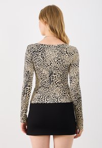 Dugih rukava majica s bež i crnim uzorkom leopard printa, sa prilagođenim dizajnom i okruglim izrezom. Uparen s crnom mini suknjom.