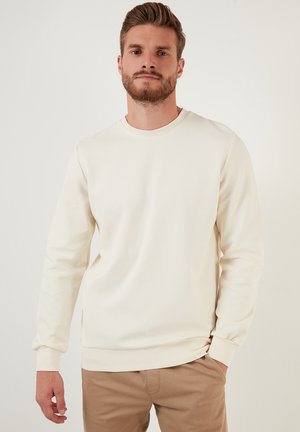 Cream-colored sweatshirt with a round neckline, long sleeves, and ribbed cuffs. Soft, textured fabric with a relaxed fit.