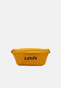 Borsa in tessuto giallo senape di Levi's con scritta nera del logo e un piccolo tag rosso sul lato sinistro, su sfondo bianco.