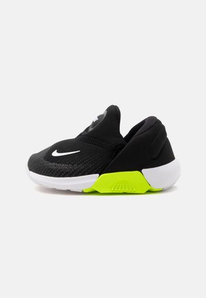 Čierna nízka športová obuv s bielou podrážkou, bielym logom Nike vpredu a jasne žlto-zeleným akcentom na medzipodošve.