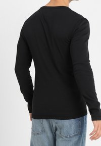 Schwarzes Langarmshirt mit Rundhalsausschnitt und glatter Textur, kombiniert mit hellblauen Jeans.