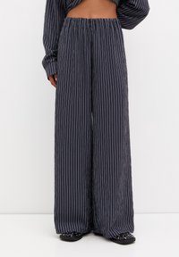 Spodnie o szerokich nogawkach w granatowym kolorze z białymi pionowymi paskami. Wykonane z lekkiego materiału, z elastycznym pasem dla wygody.