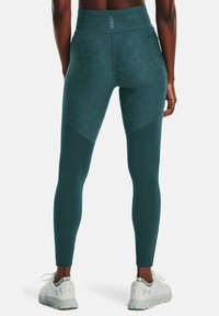 Höga turkosa leggings med texturerat mönster, sidpaneldetaljer och perforeringar för andningsförmåga. Tillsammans med vita träningstoftor.