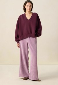 Sweat-shirt oversize bordeaux avec un col en V et un ourlet élastique, associé à un pantalon large en velours côtelé lilas clair avec des côtes verticales.