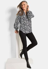 Langärmlige Bluse mit marineblauem und weißem geometrischen Muster, mit Kragen und Knopfdetail, kombiniert mit schwarzen eng anliegenden Hosen und Absatzstiefeln.