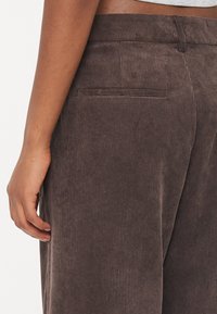 Bruine corduroy broek met een aansluitende tailleband, zijzakken en een verticale ribbelstructuur. Close-up van het detail van de achterzak.