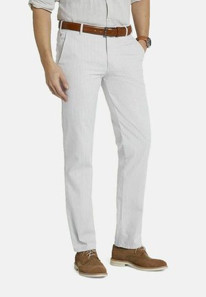 Mann, der hellgraue, fein gestreifte Hosen, braunen Ledergürtel, beige Wildleder-Brogue-Schuhe und ein hellgraues, hochgekrempeltes Hemd trägt.