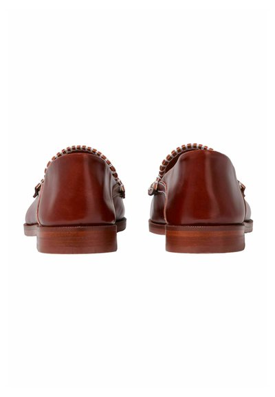 Mocasines de cuero marrón con tacón plano, punta redondeada y un borde decorativo trenzado. La suela está ligeramente elevada con un acabado liso.