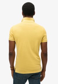 Polo shirt giallo con colletto, maniche corte e spacchi laterali, abbinato a jeans in denim scuri. Tessuto dalla superficie liscia.