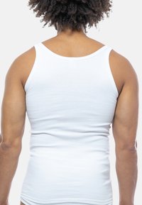 Top a canotta bianco rigato con spalline larghe. Il retro presenta un design aderente e una texture liscia, enfatizzando la silhouette.