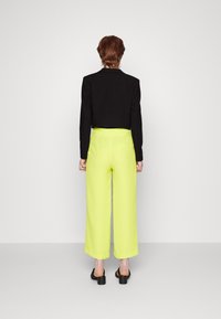 Czarna krótka kurtka z długimi rękawami w połączeniu z jaskrawożółtymi spodniami o szerokich nogawkach, charakteryzująca się gładką fakturą i minimalistycznym designem.