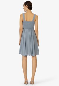 Un vestito azzurro chiaro con un corpetto arricciato e bretelle larghe, con una gonna svasata e un tessuto morbido e fluente che arriva sopra le ginocchia.