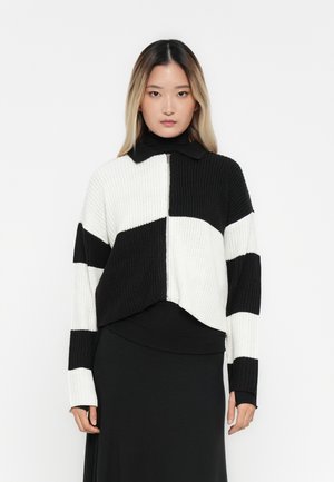 Cardigan a maglia nera e bianca a maniche lunghe, con cerniera frontale, caratterizzato da un design a blocchi di colore e una texture a coste. Collo alla coreana.