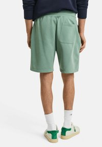 Shorts de sport vert menthe avec une texture lisse, une taille élastique et une poche arrière. Portés avec des chaussettes blanches et des baskets avec des accents verts.