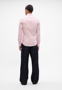 Herren Langarmhemd mit rosa Streifen und klassischem Kragen, kombiniert mit weit geschnittenen dunklen Jeans. Glatter Stoff mit Knopfdetails.
