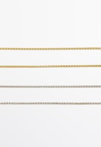 Quattro catene esposte: le due superiori in oro, le due inferiori in argento. Ogni catena presenta un design attorcigliato con una texture liscia.