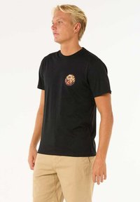 Camiseta negra de manga corta hecha de algodón, con un gráfico redondo y colorido en la parte izquierda del pecho. Diseño simple con cuello redondo.